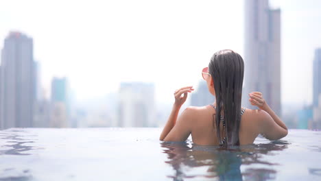 Rückansicht-Einer-Sexy-Frau-Mit-Nassen-Haaren-Im-Infinity-Pool-Auf-Dem-Dach-Mit-Modernem-Stadtbild-Im-Hintergrund