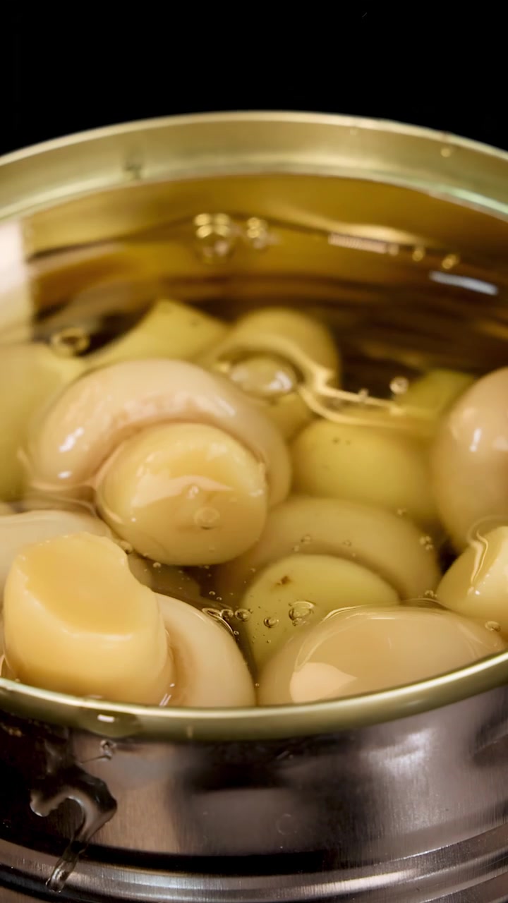 Funghi champignon interi in salamoia all'interno di una lattina di metallo aperta, con goccioline d'acqua che schizzano e creano increspature sotto una luminosa illuminazione da studio.