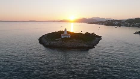 Aerial-parallax-pullback-as-sunlight-illuminates-ocean-with-pink-yellow-hues,-Alcanada-lighthouse