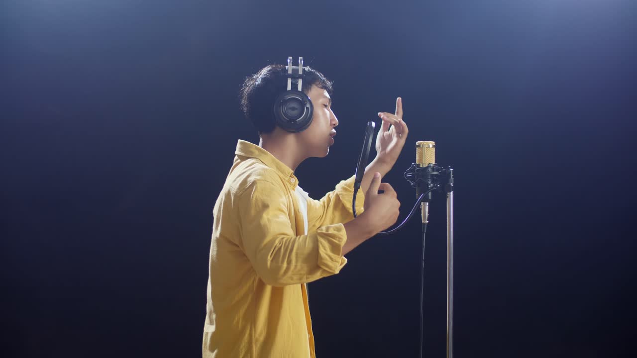 하 연기 검은 배경에 콘덴서 마이크로 하는 헤드폰을 가진 젊은 아시아 소년의 측면 시각