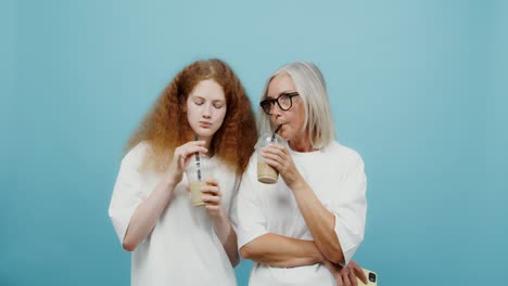 abuela y nieta compartiendo una bebida y usando un teléfono inteligente