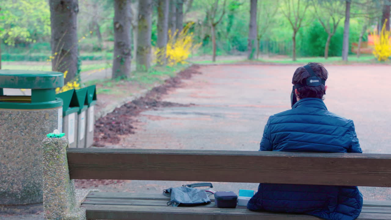 fpv googles를 착용한 남자의 중간 샷이 숲 속의 벤치에서 작은 tinywhoop 드론을 촬영합니다.