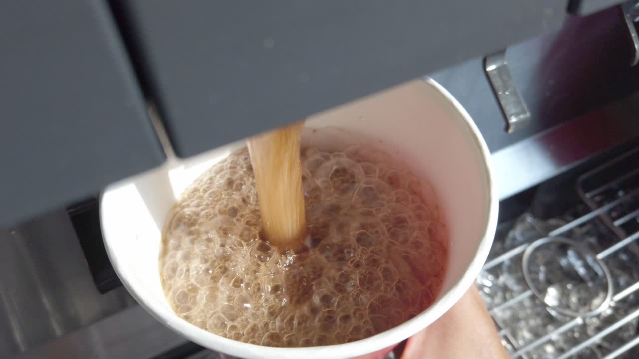 Close shot of soda being dispensed into a paper cup with ice cubes, creating foam and bubbles at the top