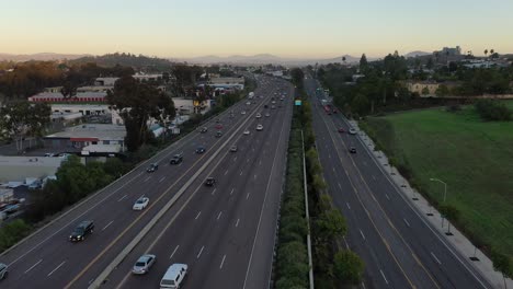 Drone-flies-over-a-busy-highway,-capturing-stunning-views-of-town-as-the-sun-sets