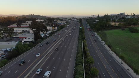 Drohne-Fliegt-über-Eine-Stark-Befahrene-Autobahn-Und-Fängt-Einen-Atemberaubenden-Blick-Auf-Die-Stadt-Ein,-Wenn-Die-Sonne-Untergeht