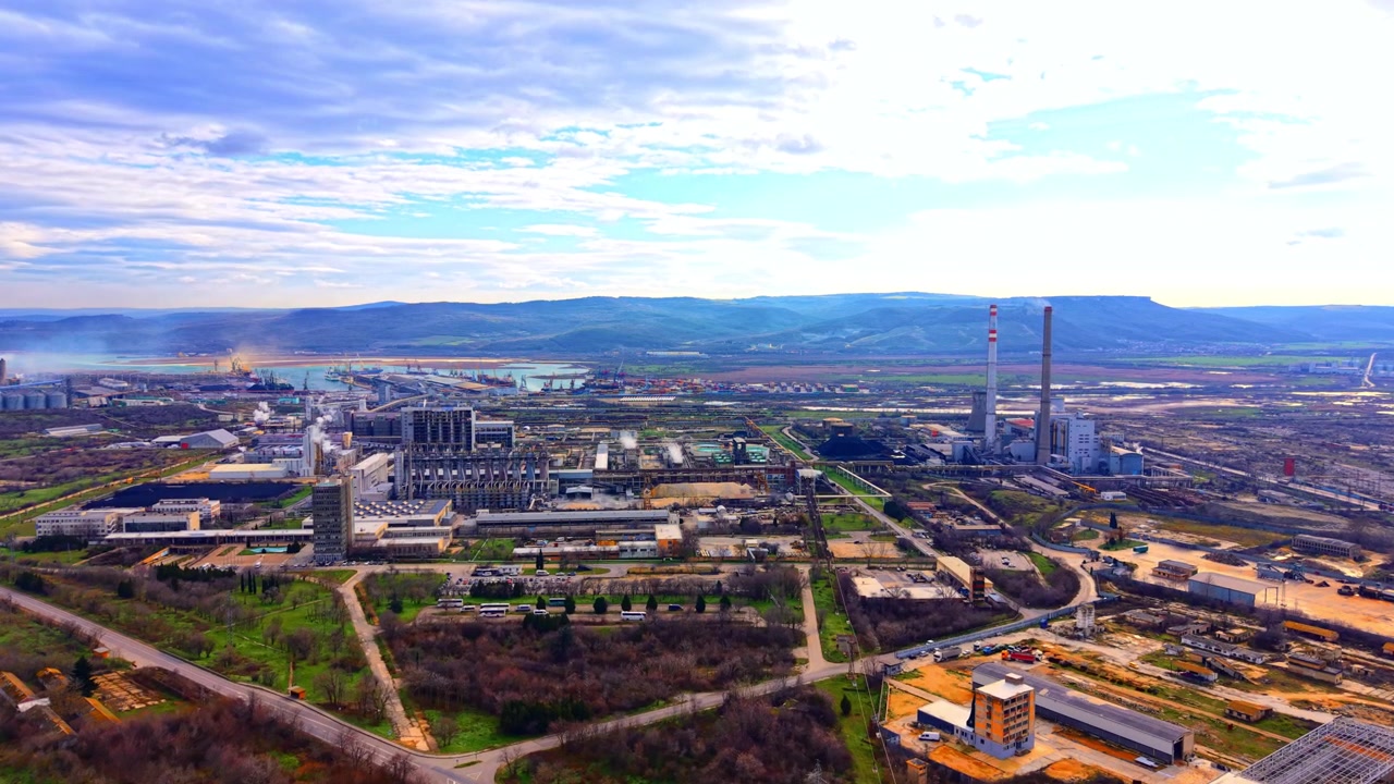 Bulgaristan, enerji santralli endüstriyel liman bölgesi. Bulutlu gökyüzü altında, uzun çizgili bacaları, kargo limanı, depoları ve yeşil alanlarıyla büyük bir kimyasal ve enerji kompleksinin geniş havadan görünümü.