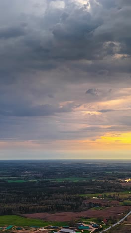 sunset glow over farmland and scattered forests with warm orange tones in sky, vertical aerial establishing