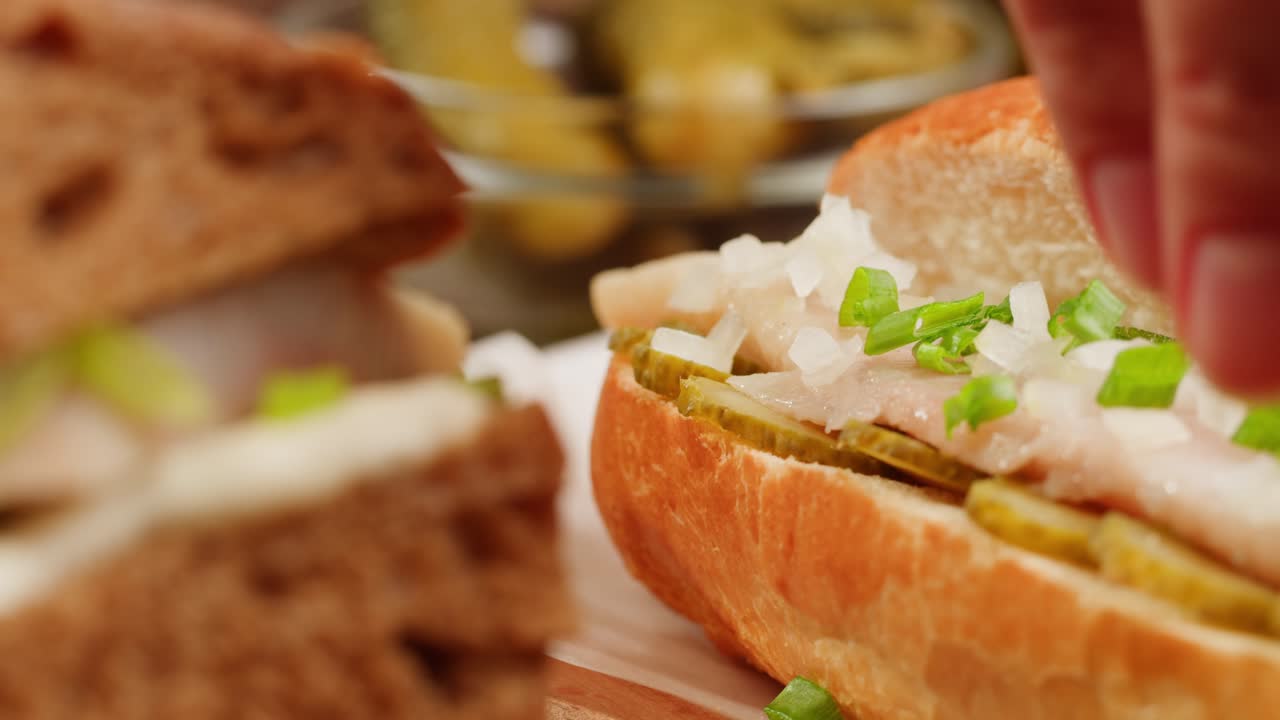 Hand placing spring onions on top of a herring sandwich