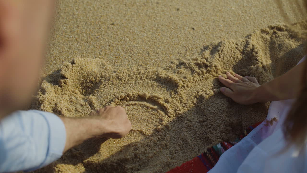 모래 에 심장 을 그리는 젊은 부부