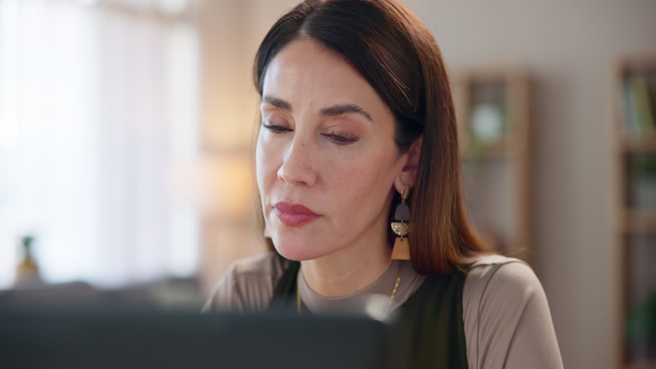 una mujer trabajando en su computadora portátil en su escritorio, mirando enfocada y concentrada.