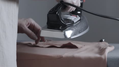 manos planchando una camisa en una tabla de planchar