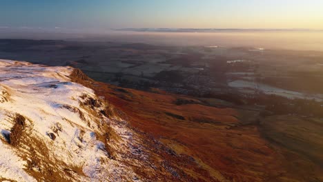 4k aerial pan from snowy cliffs of camspie fells towards countryside during sunset