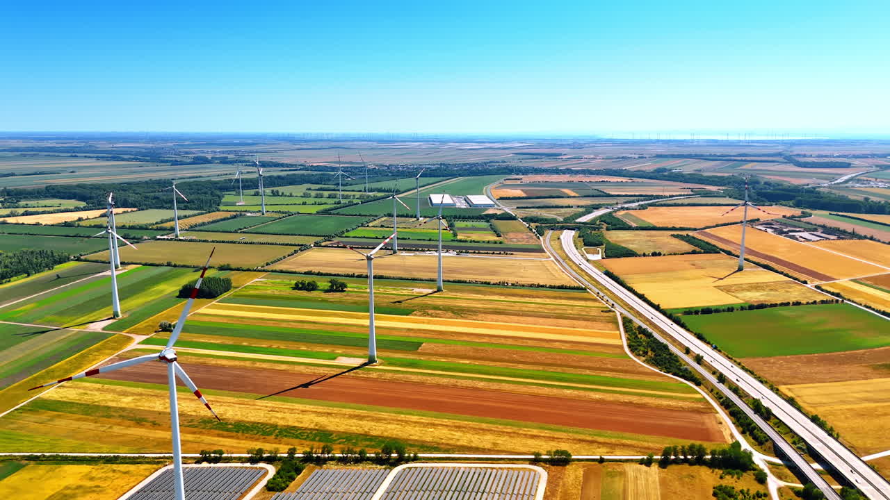 Wind turbines in vast fields. Wind turbines stand tall in a colorful landscape of fields and solar panels under a bright blue sky