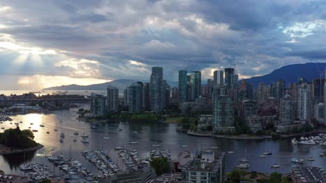 moody sunset with sun rays peaking between clouds - drone aerial shot over the vancouver marina