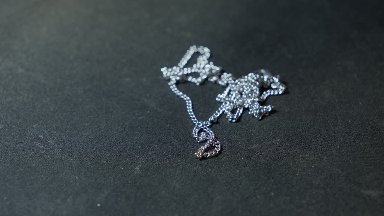 Mani posano una catena d'argento su un telo nero, texture contrastanti in una composizione elegante