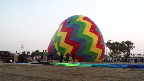 hot air balloon on its side while being filled up and preparing for takeoff while a crowd stands watching nearby in anticipation