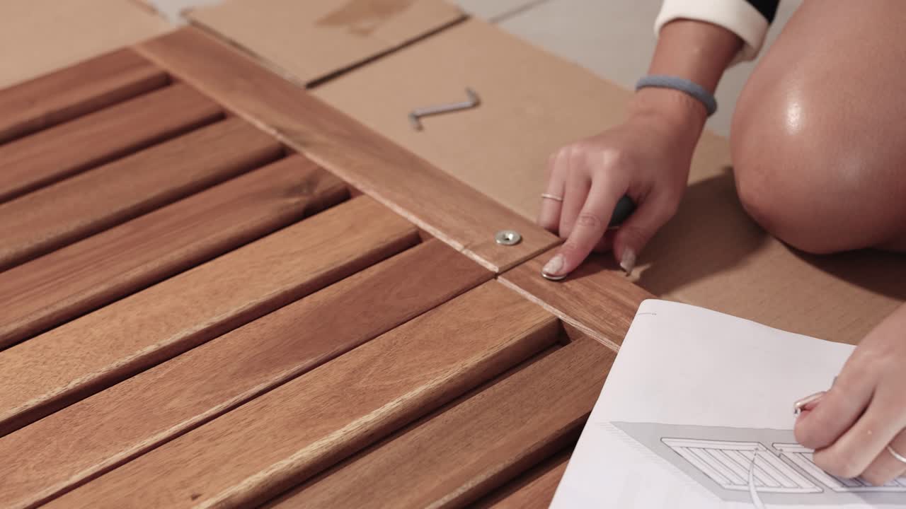 Hands assembling wooden furniture using screws and instructions. Indoor setting with natural lighting and close-up shots
