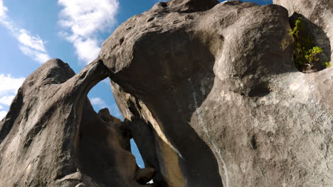 Bottom-up-shot-of-gigantic-stony-rock-formation-against-clouds-and-blue-sky