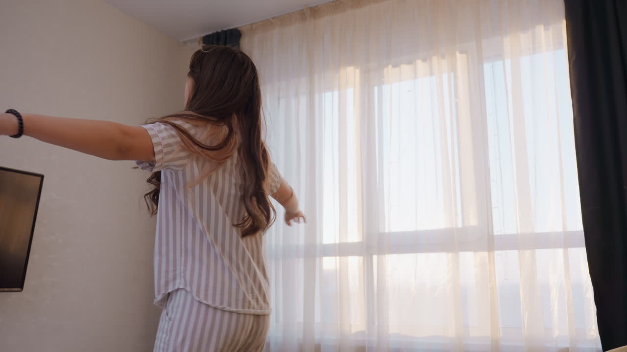Junges Mädchen streckt Hand zum Fenster, junge Frau in gestreifter Kleidung greift nach hellem Fensterlicht, energiegeladenes Mädchen in Kleidung spielt mit umgebendem Licht und Stimmung in der Nähe des Fensters