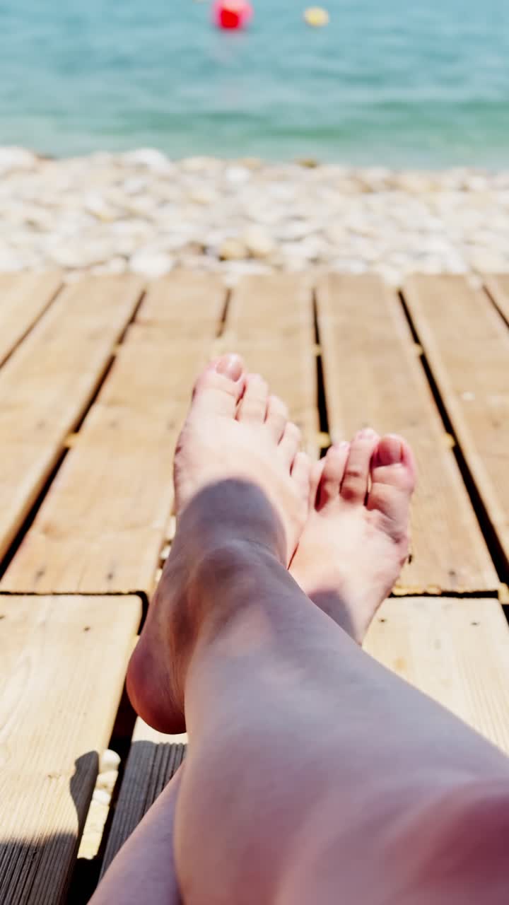 Piedi che si rilassano su un ponte di legno in riva al mare in una giornata di sole