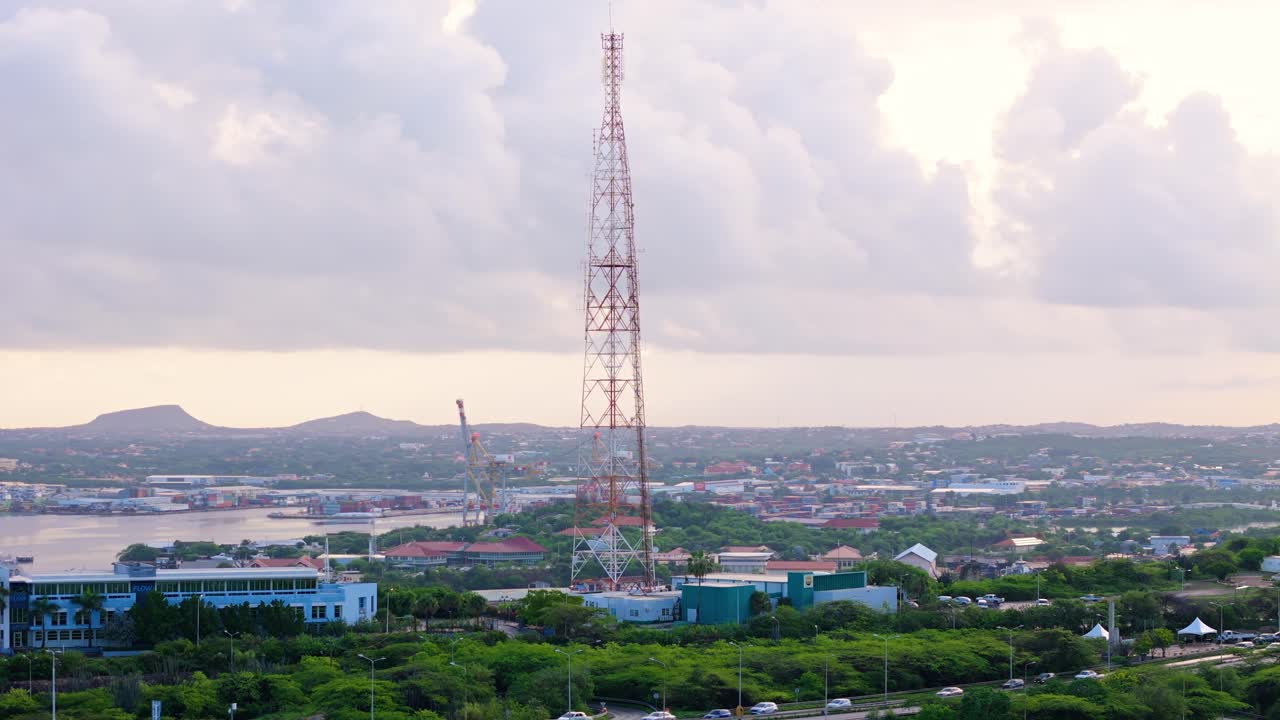 커다란 통신 타워가 쿠라카오의 도시와 구름이 가득한 하늘을 가로질러 높이 아 있다.