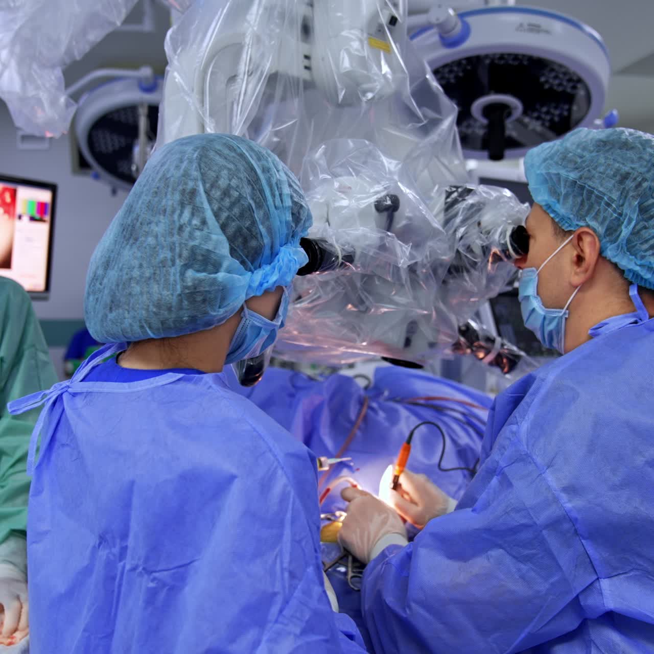 Male Caucasian surgeon performing neurosurgery assisted by male and female medics. Professional doctor looks at the microscope at operation