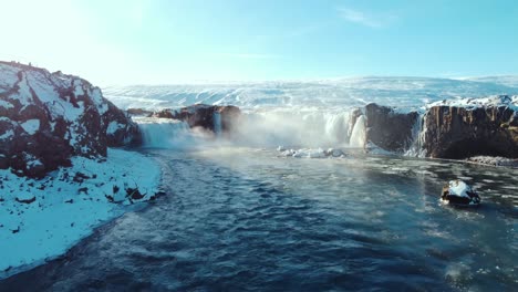 An impressive aerial drone perspective captures the powerful cascade of Godafoss waterfall amidst a snowy winter landscape