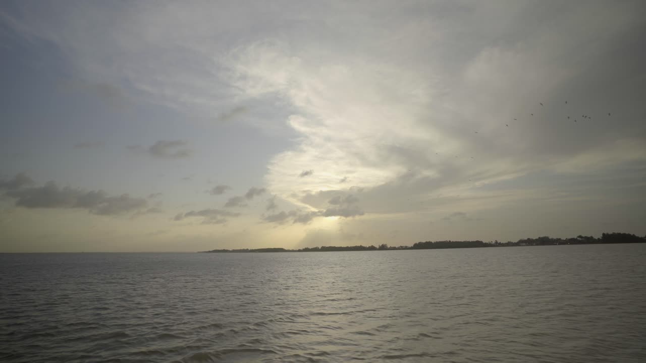 갈색, 차분하고 느리게 흐르는 평평한 강물의 넓은 낮은 각도 시각, 풍경 실루과 함께 구름이 가득한 하늘 아래의 배에서 볼 수 있습니다.