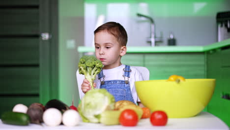 curious child examines fresh vegetables. a young child sits at a table filled with various fresh vegetables, thoughtfully holding broccoli in a bright kitchen