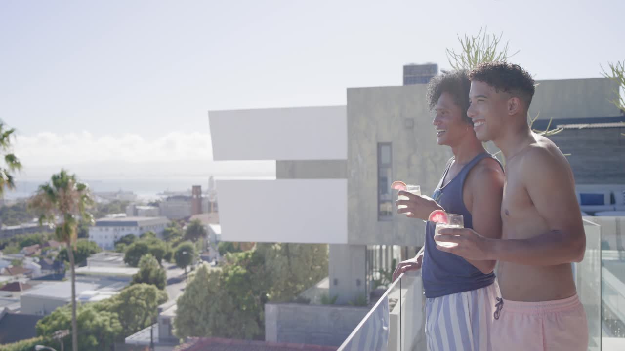 Uomini afroamericani che entrano da una porta con un drink, appoggiati alla ringhiera del balcone mentre ammirano il panorama, con spazio per il testo.