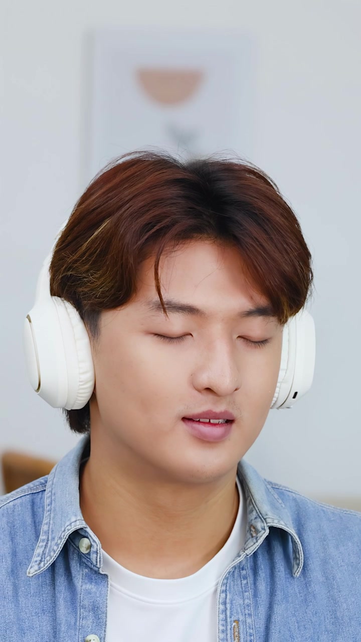Un giovane uomo asiatico indossa cuffie bianche e si gode la musica in una stanza luminosa
