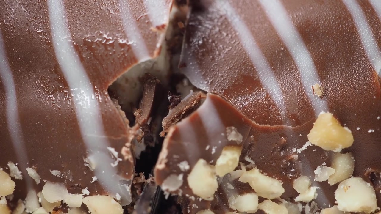Primo piano di un coltello che taglia una barretta di noci ricoperta di cioccolato.