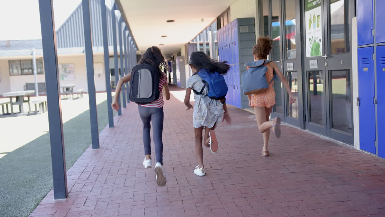 Three biracial girls are running through a school corridor