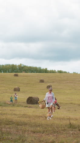 vista distante de una familia caminando con su perro a través de un campo abierto con balas de heno esparcidas, un entorno rural pacífico con niños y adultos disfrutando del tiempo al aire libre bajo un cielo nublado
