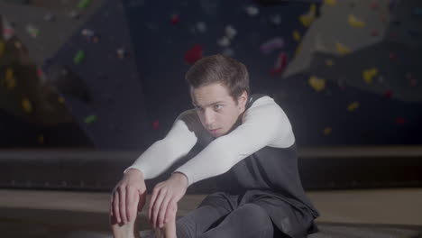 joven deportista enfocado haciendo ejercicios de calentamiento y estirando las piernas en un gimnasio de boulder