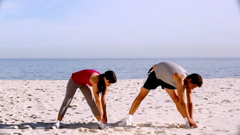 sportsman and sportswoman stretching on the beach