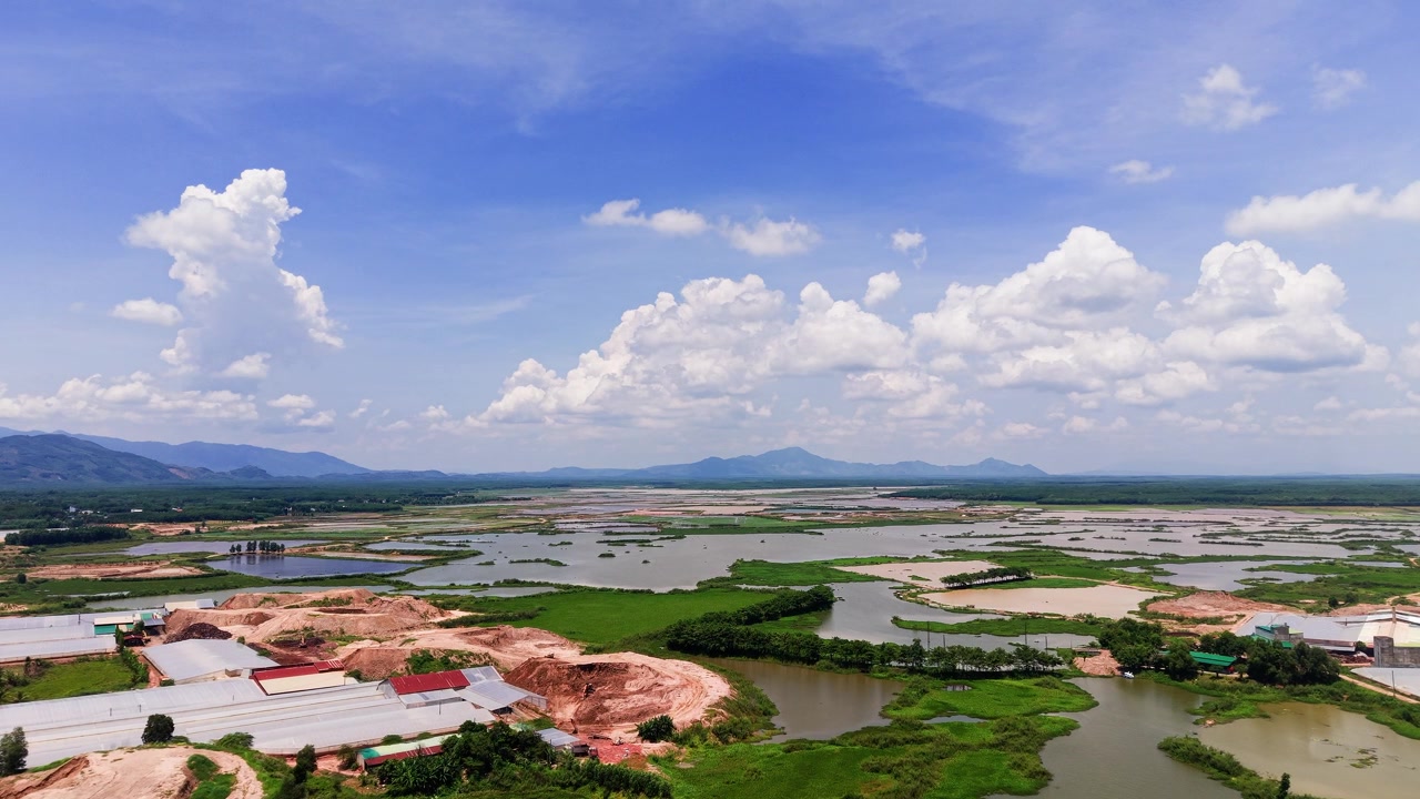 Højt over Duc Linh i Lam Dong, Vietnam, viser landskabet marker og floder. Skyer fylder himlen. Udsigten fanger naturen og landlivet i dette område. Solen skinner klart.