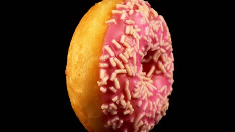 pink glazed donut with sprinkles on black background.