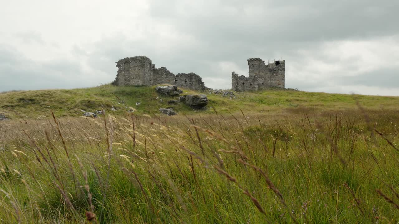 Ancient stone ruins on a grassy hill under a cloudy sky, captured in a wide shot