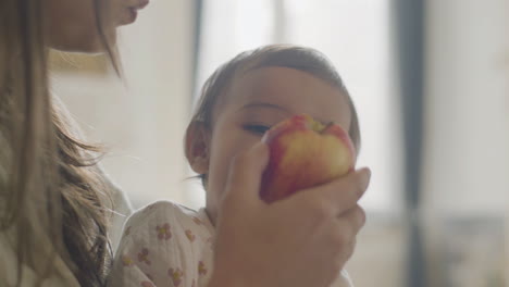 close up of a mom holding her baby daughter and eating an apple together on the morning