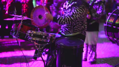 musician in costume playing drum kit in real time on stage with band under party lights