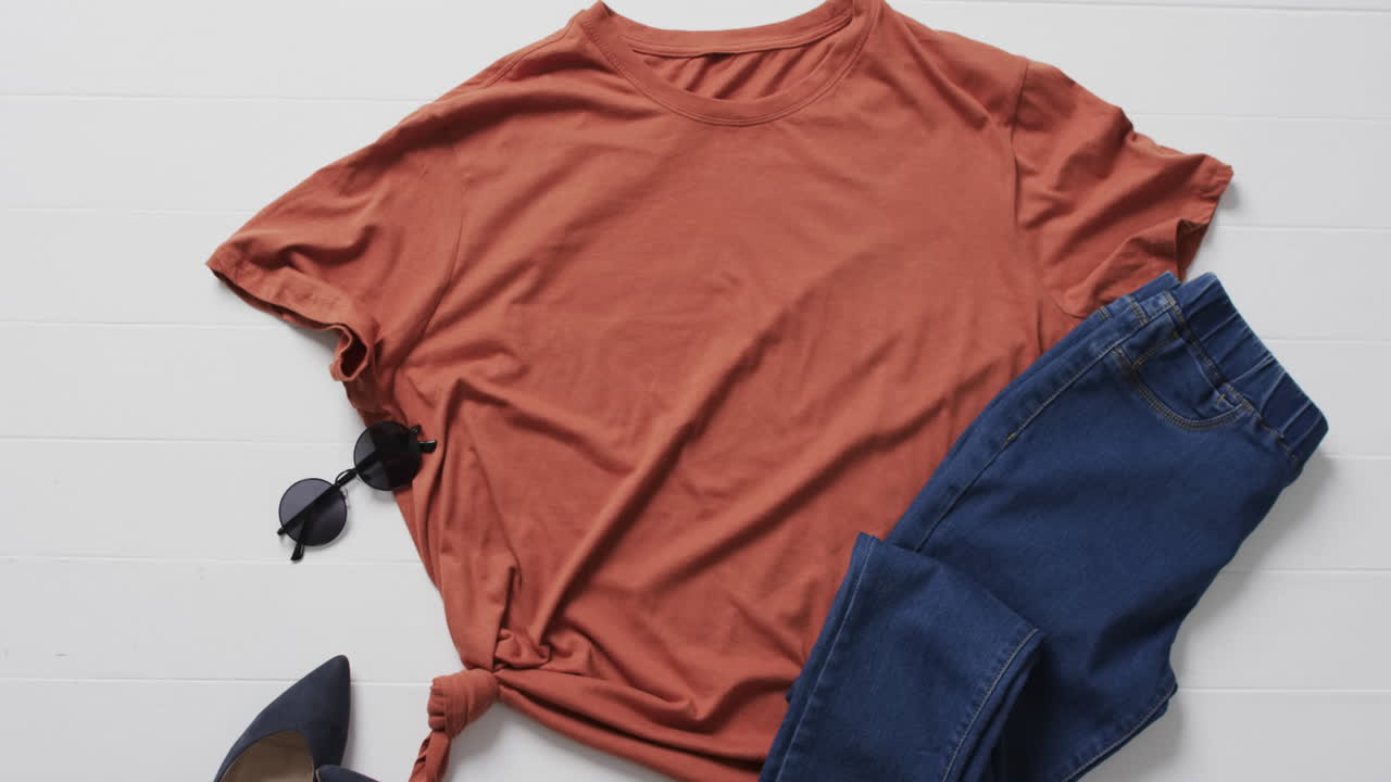 Video of orange t shirt, denim trousers, sunglasses and copy space on white background