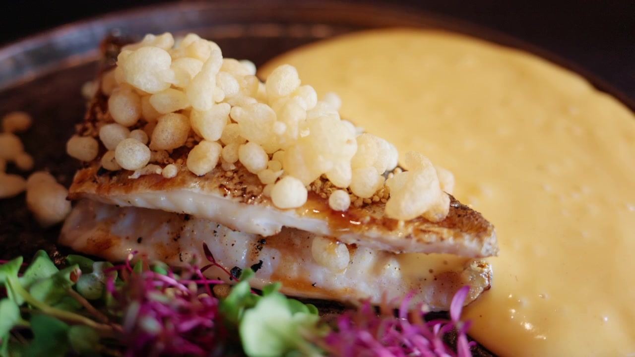 Close up of a gourmet fish dish with creamy sauce, pine nuts, and colorful microgreens