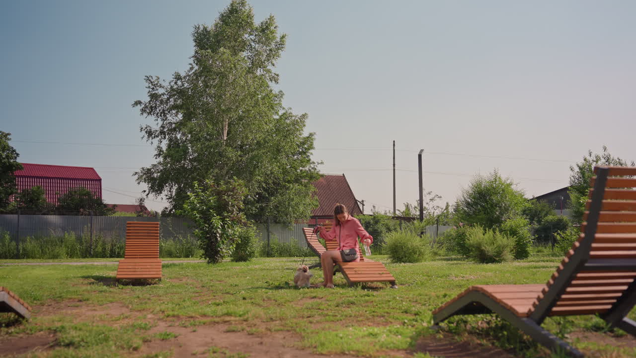 Caucasian Woman Garden Dog Walking Slow, Relaxed Homeowner Stroll Between Wooden Loungers, Sunny Grass, Distant Cottages, Small Fluffy Dog Following Closely, Soft Cinematic Light, Peaceful Summer Mood