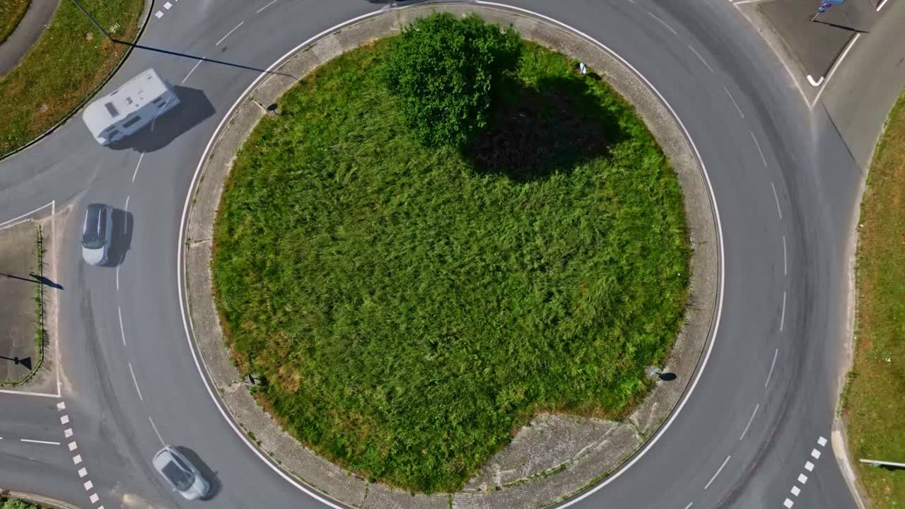 Top-down hyperlapse drone view of traffic roundabout with cars and green central island in the middle.