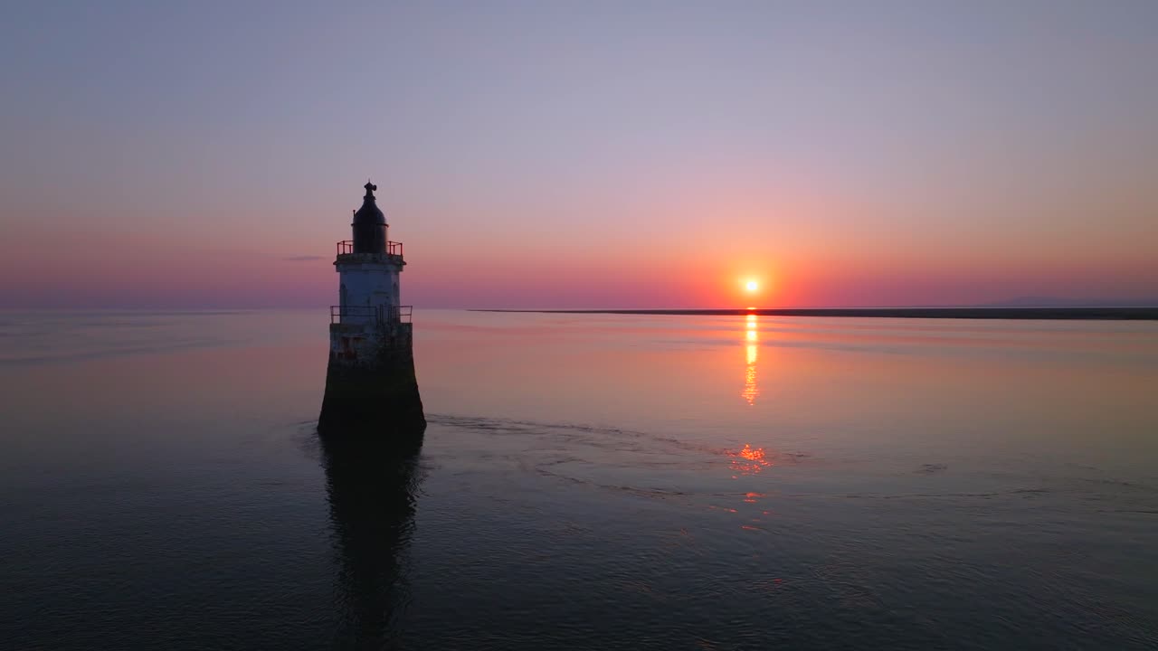 Old derelict Lighthouse in very calm waters with sunset reflecting. Stationary shot. Plover Scar Lighthouse, Lancashire, UK.