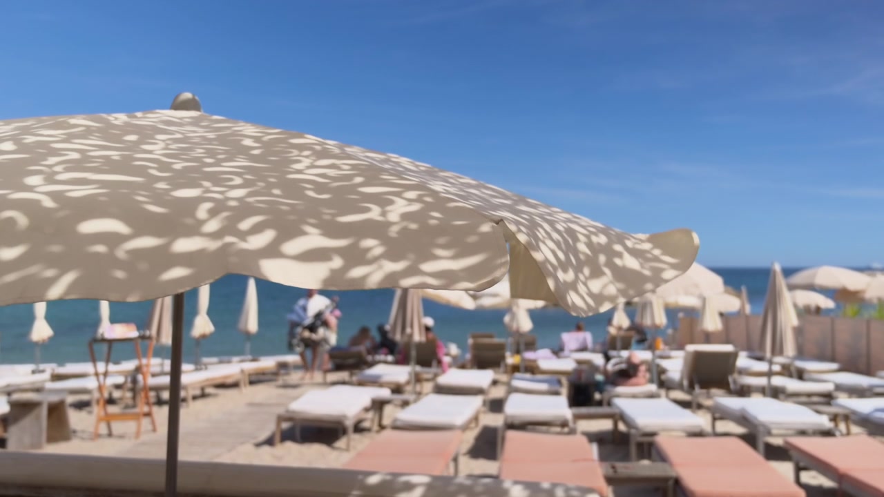 Vista con effetto soft focus di un resort di lusso fronte mare, con file di lettini, ombrelloni decorativi e vista sul mare scintillante.