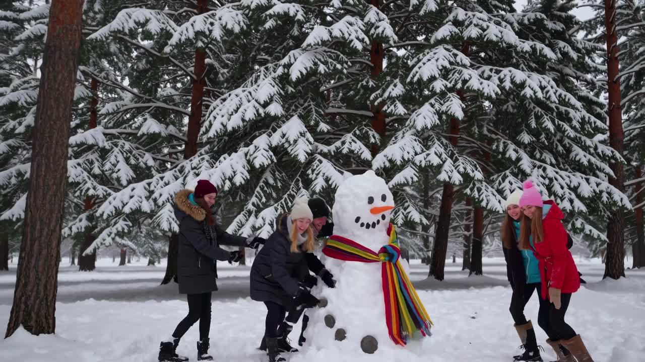 A lively group poses with a snowman in a snowy forest. Captured from a front angle, the video