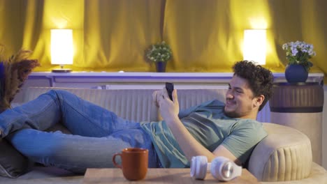 el hombre acostado en el sofá está usando el teléfono. postura agradable y cómoda.
