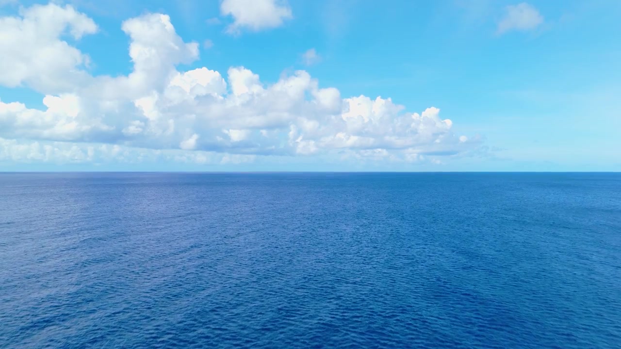Carrellata aerea bassa e veloce si alza sopra l'acqua blu dell'oceano con leggere increspature sotto un cielo luminoso, sfondo naturale sereno